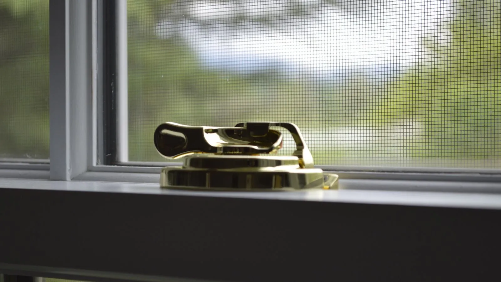 Window latch with a mesh screen behind it, illustrating security screens for windows